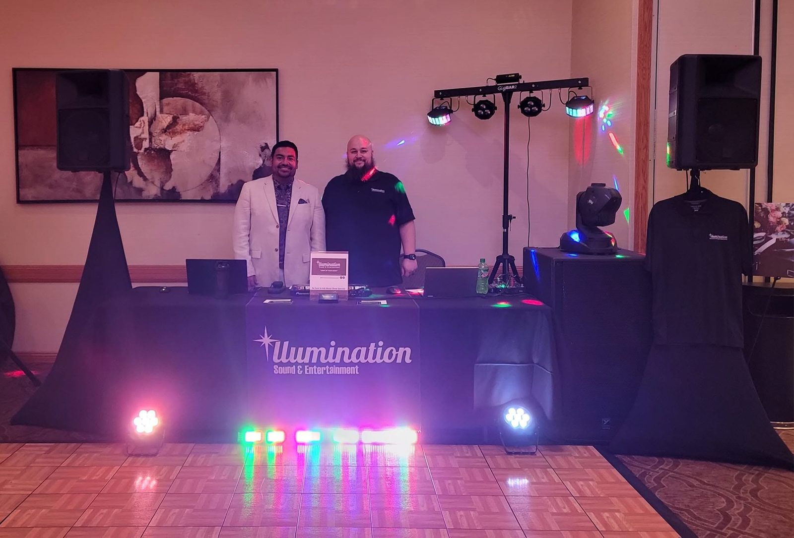 Andrew Miller and David Webster of Illumination Sound & Entertainment behind their DJ table with speakers and party lights